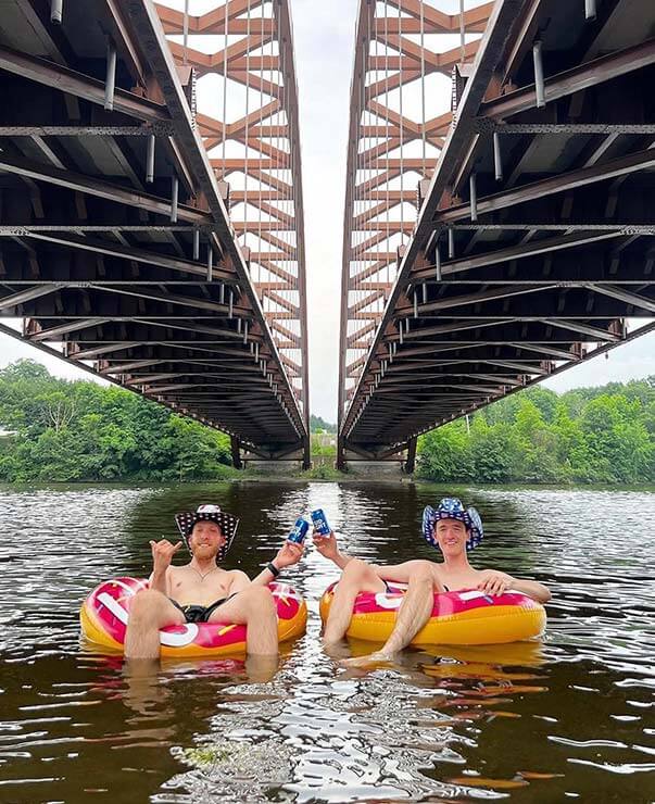 Two men in tubs floating on a river under two bridges